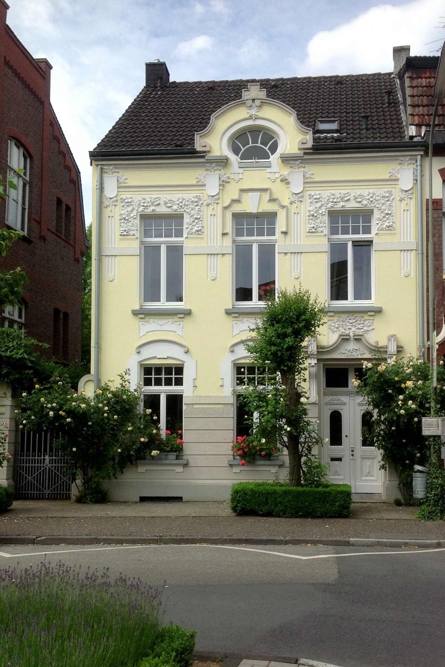 buero-westwall-37-geldern Bürogebäude am Westwall 37 in Geldern: hellgelbe Jugendstilfassade mit weißem Stuck, Rundfenster im Giebel und Rosen am Eingang