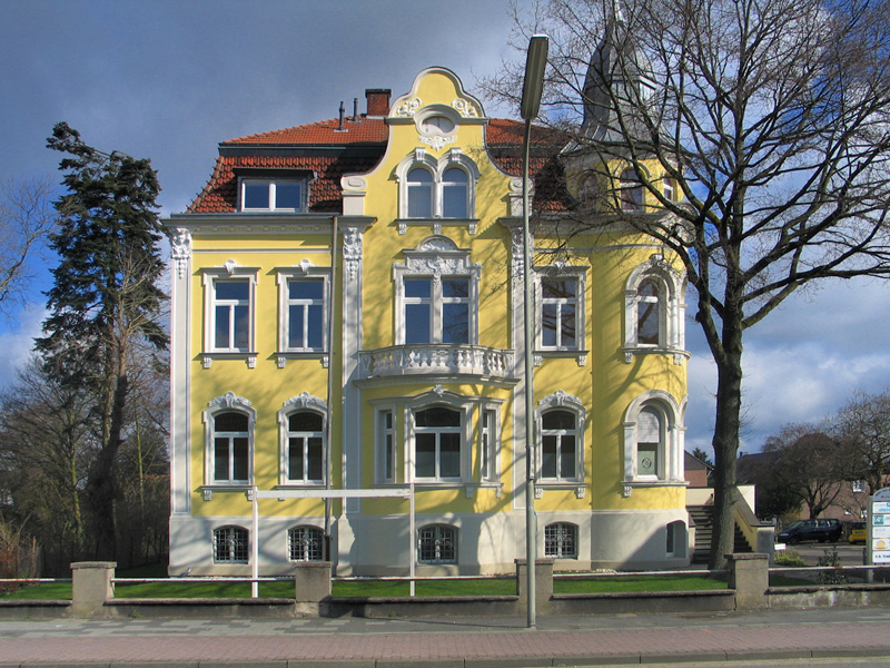 Gelbe Gründerzeitvilla mit weißem Stuck, Erker, Balkon und geschwungenem Giebel