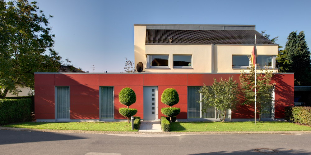 Modernes Haus mit rotem Erdgeschoss, hellem Obergeschoss und Flachdach, Kugelbäume am Eingang