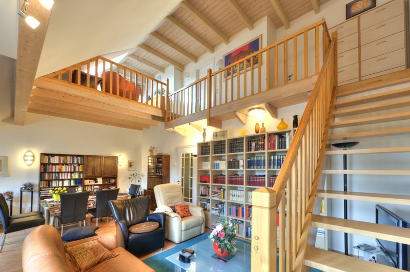 Wohnraum mit Holztreppe zur Galerie, Bücherregalen und Holzbalkendecke