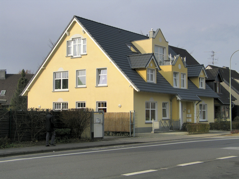 Gelb verputztes Mehrfamilienhaus mit Zwerchgiebeln, Gauben und weißen Sprossenfenstern