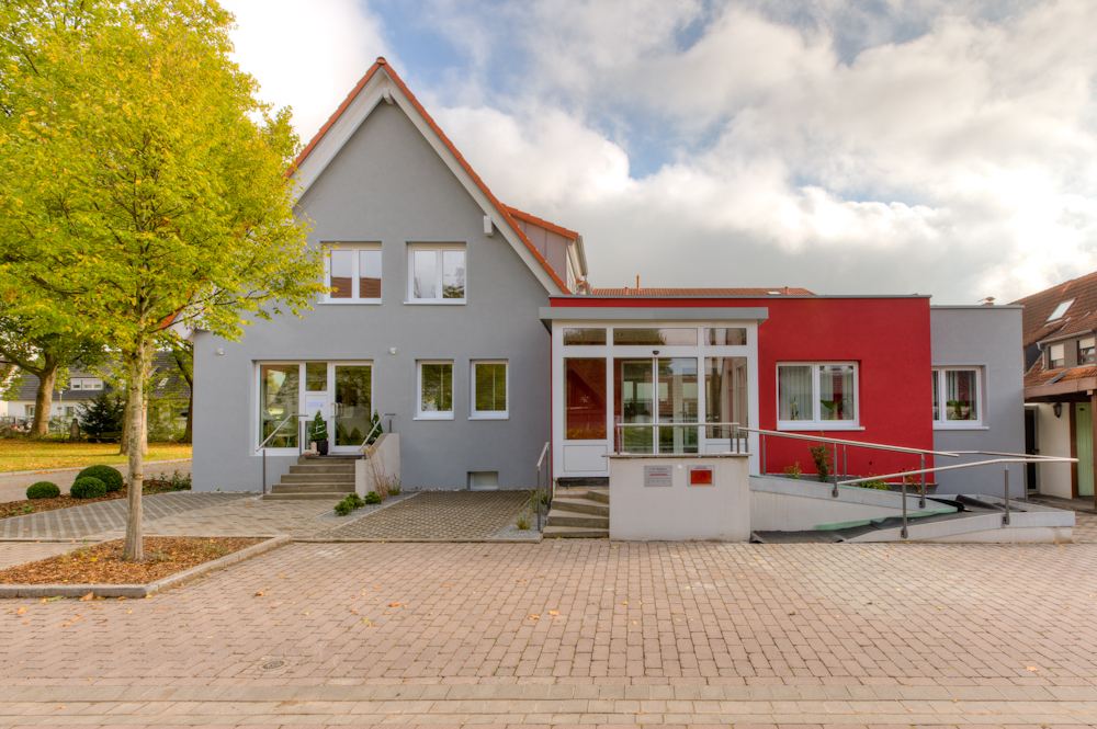 Giebelansicht mit verglastem Eingangsvorbau, rotem Anbau und Rampe