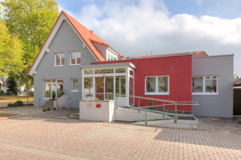 Giebelhaus mit verglastem Windfang, rotem Anbau und barrierefreier Rampe mit Geländer